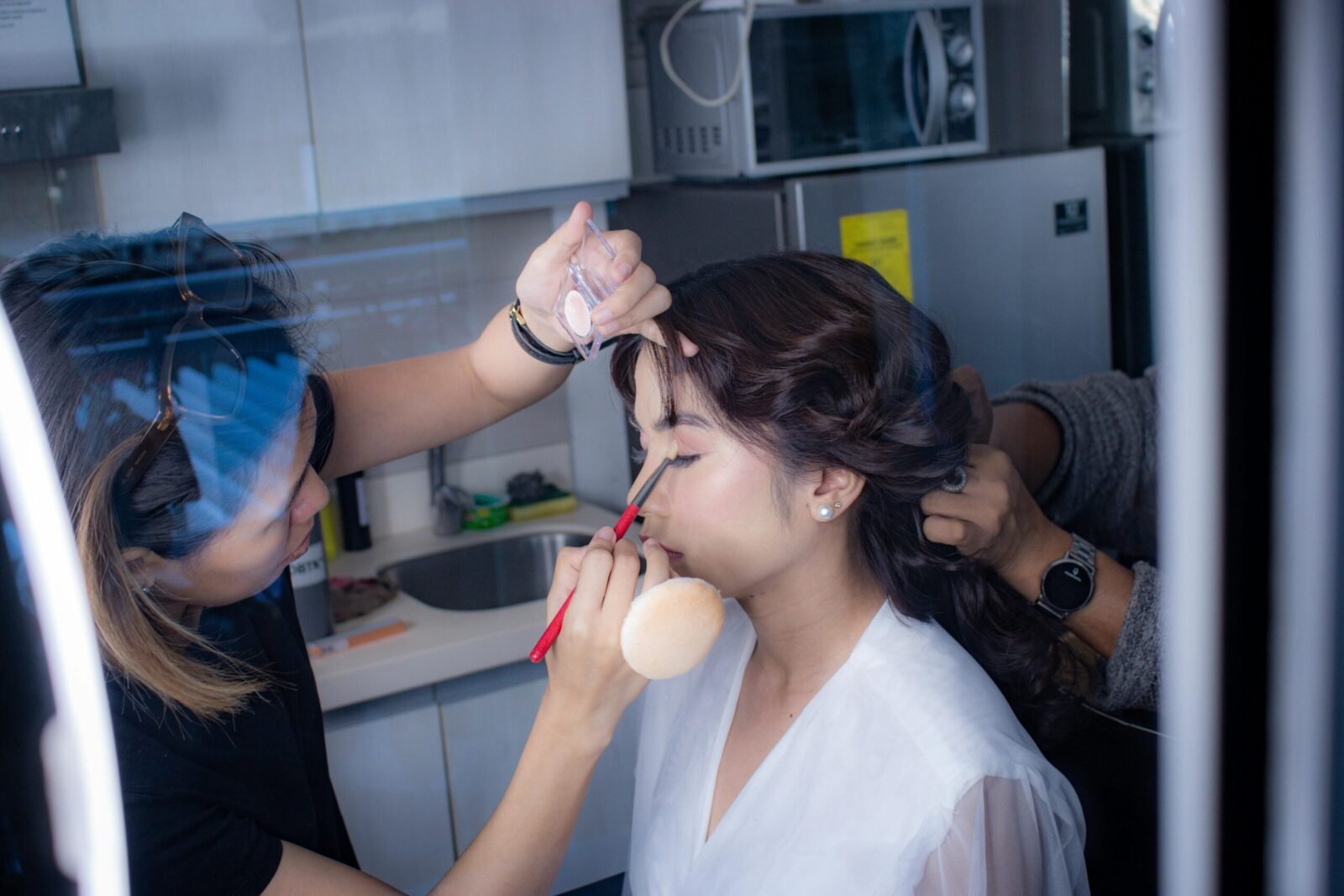 Bride getting her makeup done by beautician for wedding day preparation in salon.