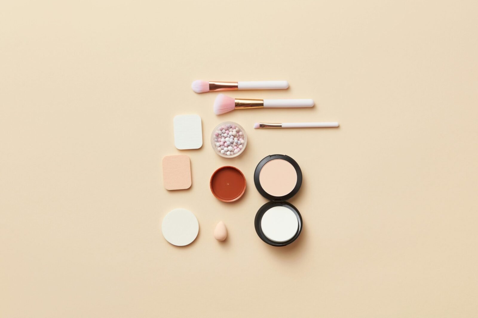 A flat lay of makeup brushes and cosmetics on a beige background, perfect for beauty themes.