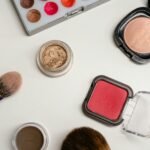 Flat lay of various makeup products including brushes, powders, and creams on a white surface.